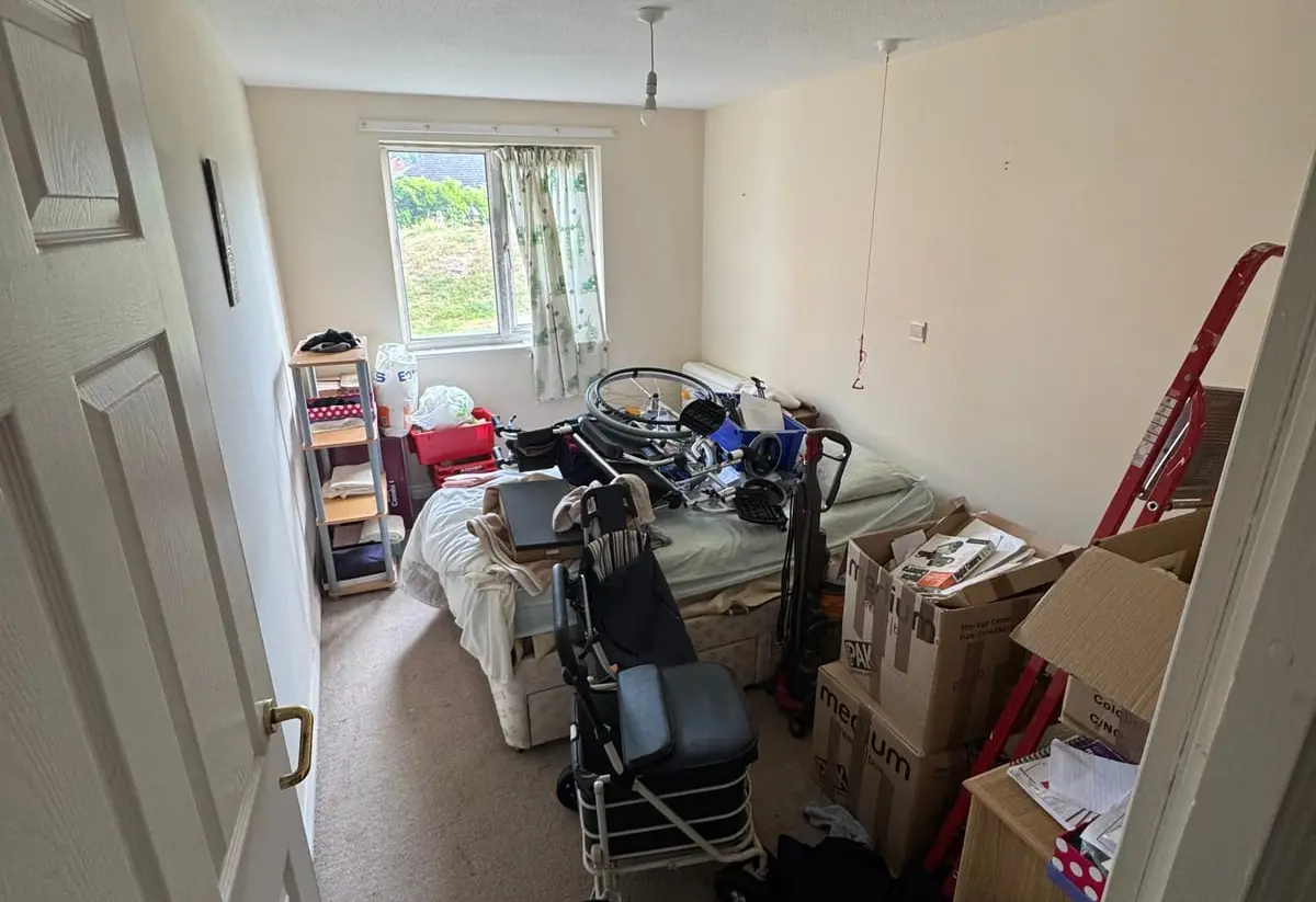 A bedroom with cardboard storage boxes stacked beside the bed, part-way through being sorted