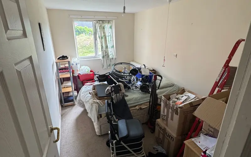 A bedroom with cardboard storage boxes stacked beside the bed, part-way through being sorted